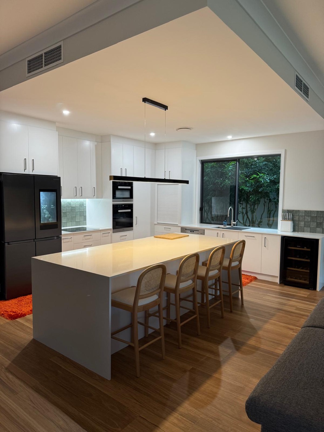 White kitchen with a large island bench, pendant lighting and black appliances
