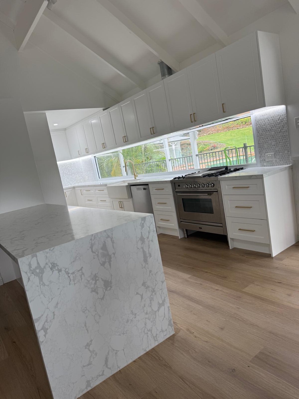 Vaulted-ceiling kitchen with a marble waterfall island and window splashback