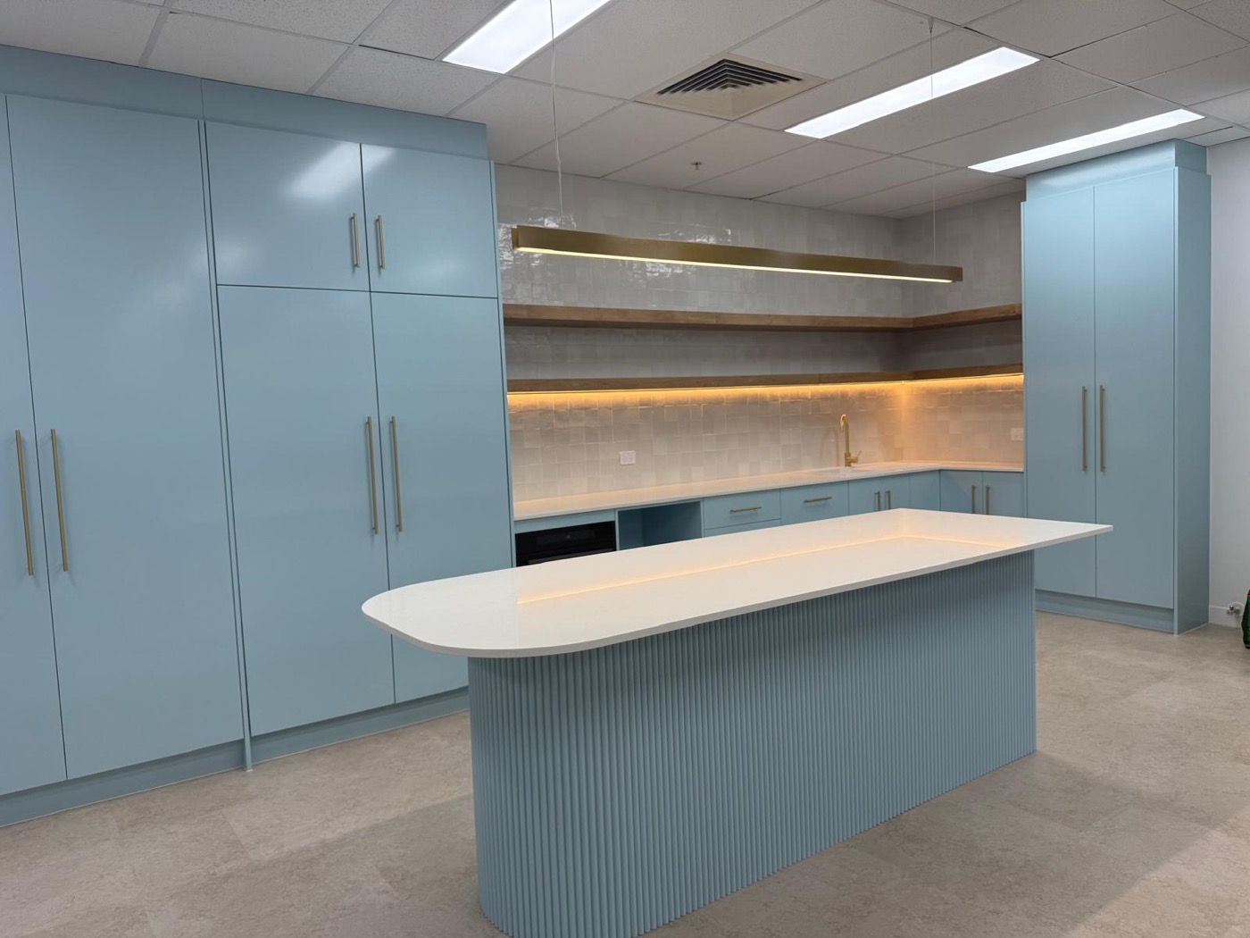 Blue kitchenette with a fluted island, timber shelving and lit splashback