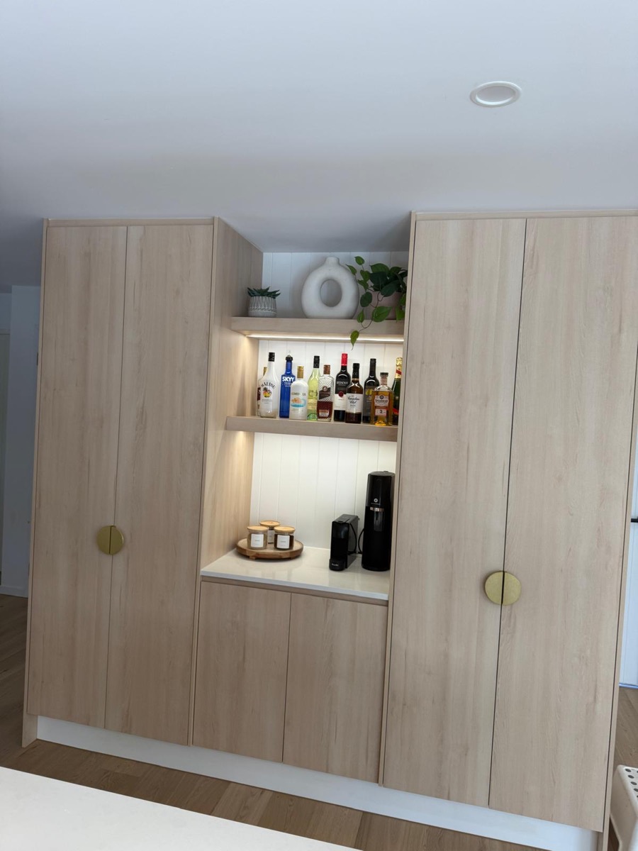 Timber-look bar cabinetry with lit display shelving and brass handles, built by Quality Cabinets